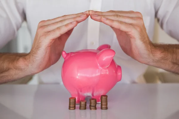 Businessman sheltering piggy bank and coins — Stock Photo, Image