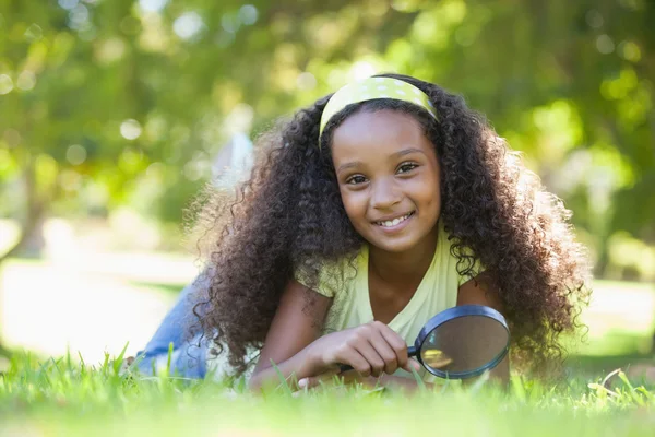 Girl holding magnifying glass in the park — Stock Photo, Image