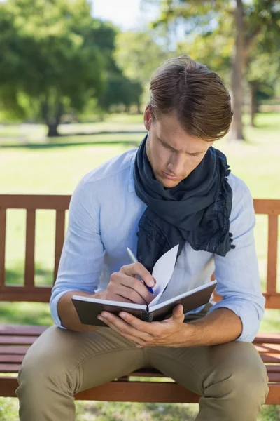Man writing in his notepad on bench — Stock Photo, Image