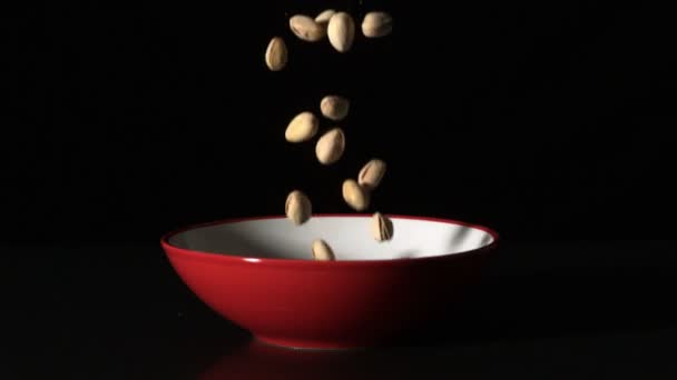 Фисташковые орехи падают в красную чашу — стоковое видео