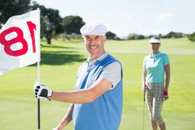 Golfer holding eighteenth hole flag with partner clipart