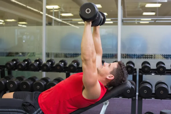 Bodybuilder lying on bench lifting dumbbells — Stock Photo, Image