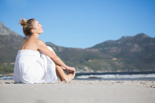 Blondine im weißen Kleid sitzt am Strand — Stockfoto