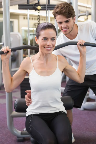 Brunette using weights machine with trainer — Stock Photo, Image