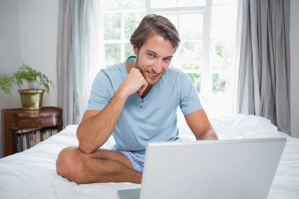 Uomo seduto sul letto con il computer portatile — Foto Stock