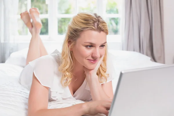 Blonde liggend op bed met behulp van laptop — Stockfoto