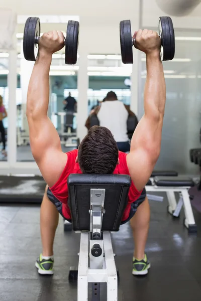 Bodybuilder lying on bench lifting dumbbells — Stock Photo, Image