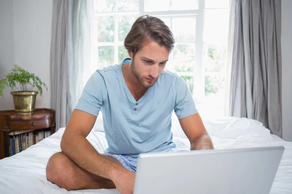Человек, сидящий на кровати с ноутбуком — стоковое фото