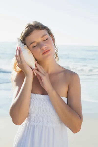 Bionda sulla spiaggia ascoltando conchiglia — Foto Stock