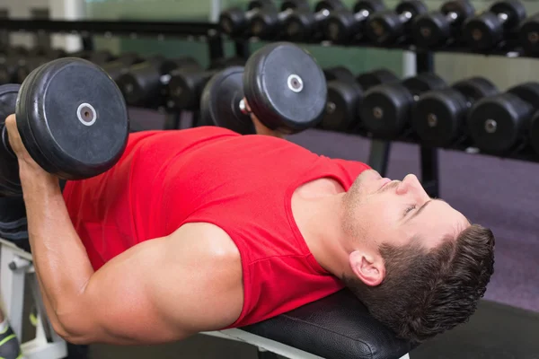 Bodybuilder lying on bench lifting dumbbells — Stock Photo, Image