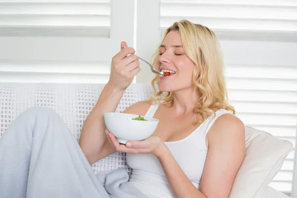 Blondynka na kanapie jedzenie sałatka — Zdjęcie stockowe
