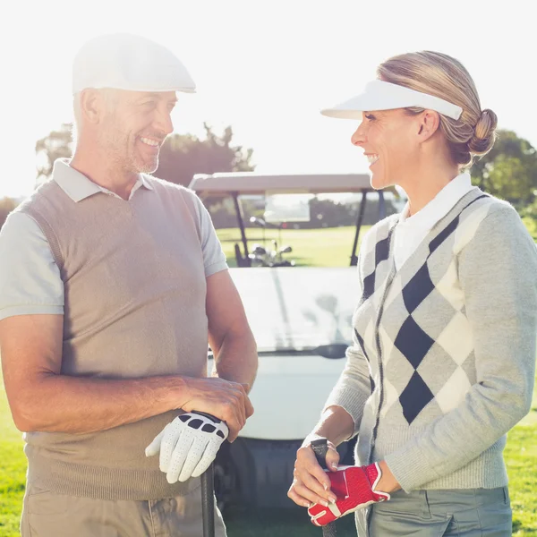 Golfing couple chatting with golf buggy behind — Stock Photo, Image