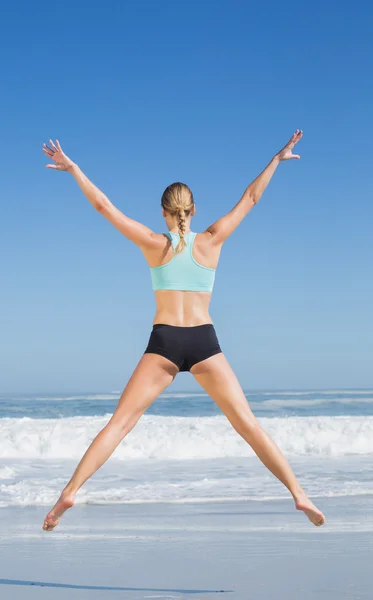 Woman jumping on beach with arms out — Stock Photo, Image