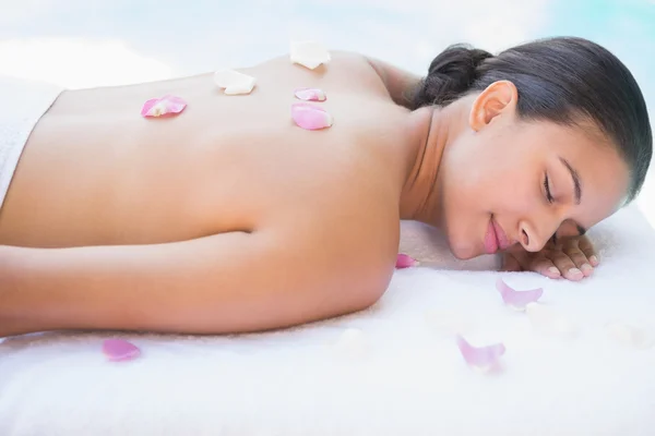 Brunette liggend op een handdoek met rozenblaadjes — Stockfoto