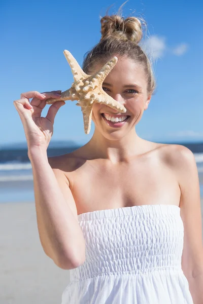 Loira segurando estrela do mar na praia — Fotografia de Stock