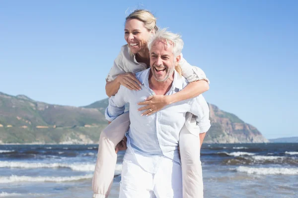 Man giving his wife a piggy back at the beach — Stock Photo, Image