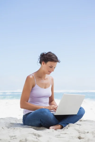 Brunette met behulp van laptop op strand — Stockfoto
