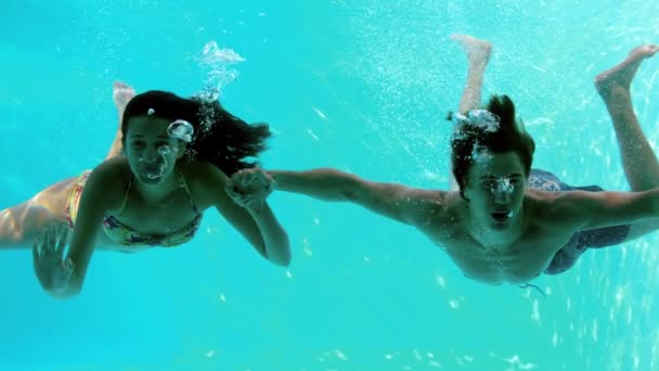 Pareja feliz cogida de la mano bajo el agua en la piscina y saludando — Vídeo de stock