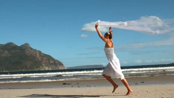 Despreocupado rubia corriendo en la playa sosteniendo bufanda hasta — Vídeos de Stock