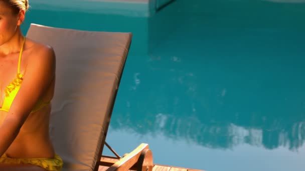 Sexy woman in yellow bikini relaxing on deck chair poolside — Stock Video