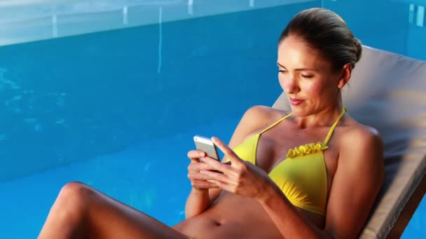 Vacker blondin i bikini SMS på telefonen vid poolen — Stockvideo