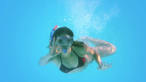 Брюнетка плавает под водой в трубке, делая хорошо знак — стоковое видео