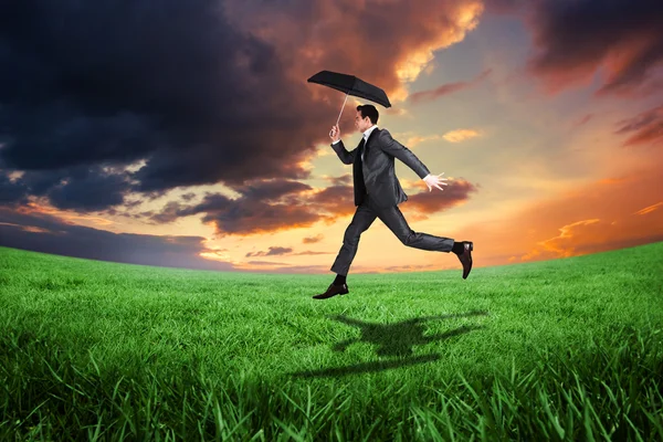Businessman jumping holding an umbrella — Stock Photo, Image