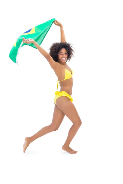 Fit dívka v žluté bikiny drží vlajky Brazílie se usmívá na kameru — Stock fotografie