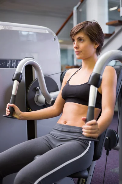 Smiling brunette using weights machine for arms — Stock Photo, Image