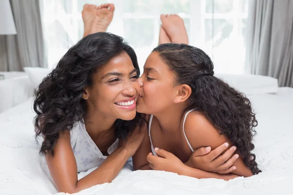 Mujer bonita acostada en la cama con su hija besando mejilla — Foto de Stock