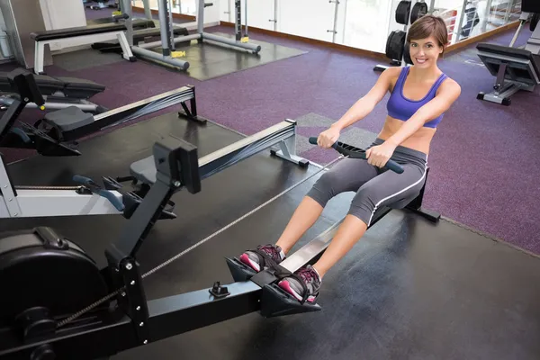 Fit morena sonriente haciendo ejercicio en la máquina de remo — Foto de Stock