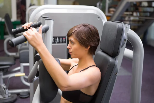 Happy brunette using weights machine for arms — Stock Photo, Image