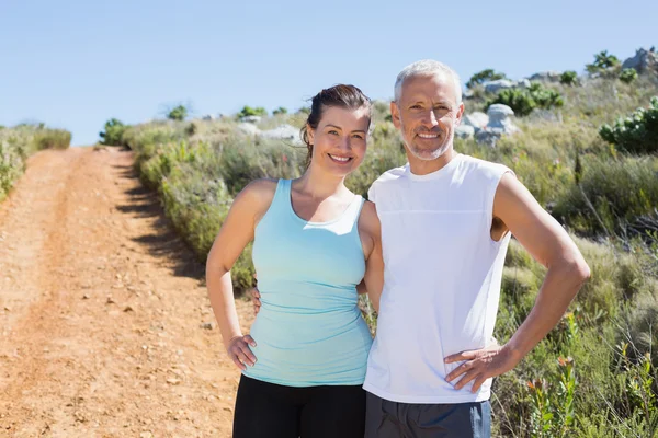 Ajuste sonriente pareja abrazando y sonriendo a la cámara en el país tr — Foto de Stock