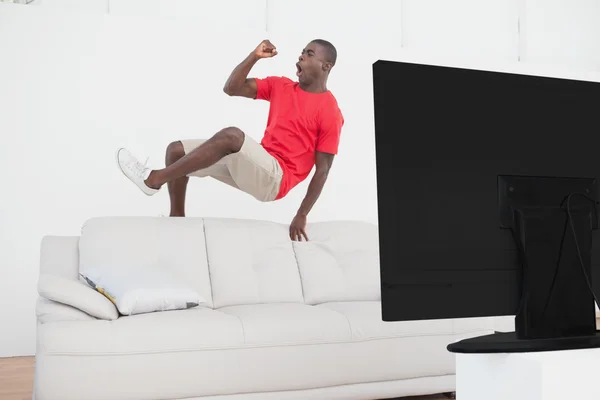 Football fan jumping over couch cheering — Stock Photo, Image