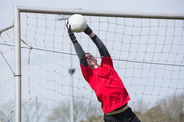 Goleiro em vermelho pulando para salvar um gol — Fotografia de Stock