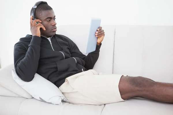 Casual man sitter på sin soffa som lyssnar på musik på TabletPC — Stockfoto