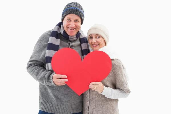 Happy mature couple in winter clothes holding red heart — Stock Photo, Image