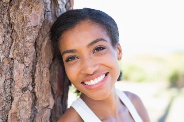 Fit woman leaning against tree smiling at camera — Stock Photo, Image