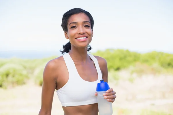 Fit mujer sosteniendo botella deportiva sonriendo a la cámara —  Fotos de Stock