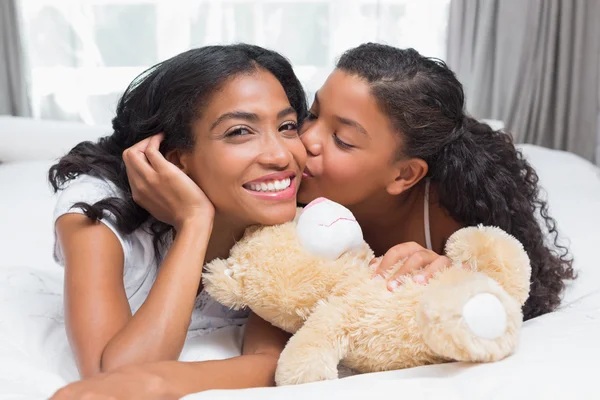 Mujer bonita acostada en la cama con su hija besando mejilla —  Fotos de Stock