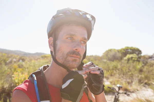 Apto ciclista ajustando alça capacete no terreno do país — Fotografia de Stock