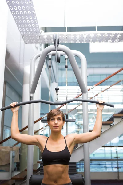 Fit brunette using weights machine for arms — Stock Photo, Image