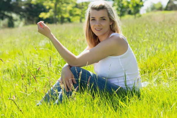 Hezká blondýnka s úsměvem na kameru sedí na trávě — Stock fotografie