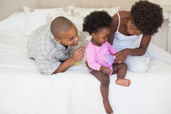 Счастливые родители и малышка сидят вместе на кровати — стоковое фото