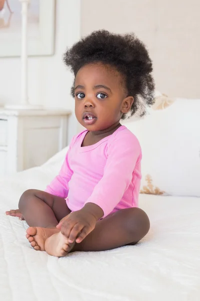 Bambina in baby gro rosa seduta sul letto — Foto Stock