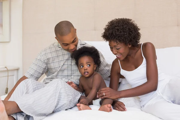 Gelukkige paar zittend op bed met baby dochter — Stockfoto
