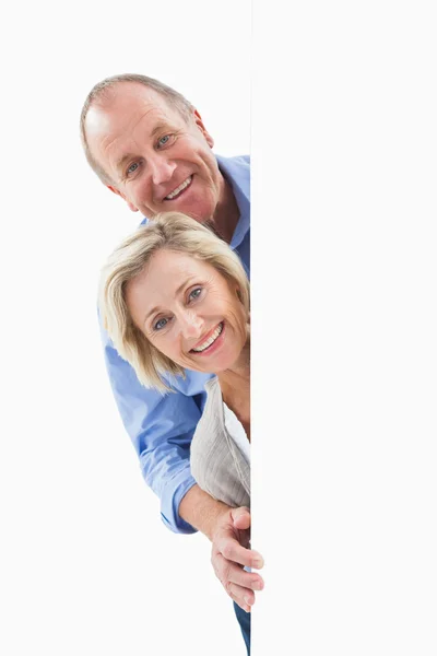 Mature couple smiling behind wall — Stock Photo, Image