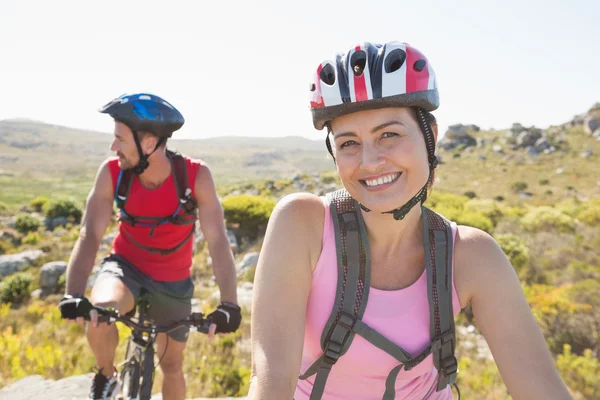 Adatto coppia ciclista sorridente alla fotocamera sul sentiero di montagna — Foto Stock