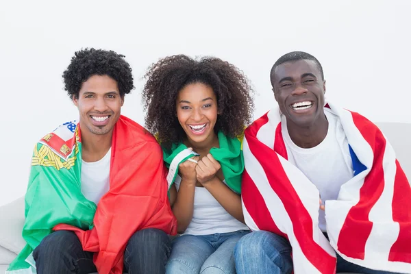 Football fans sitting on couch with flags — Stock Photo, Image