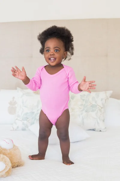 Baby girl in pink babygro standing on bed — Stock Photo, Image